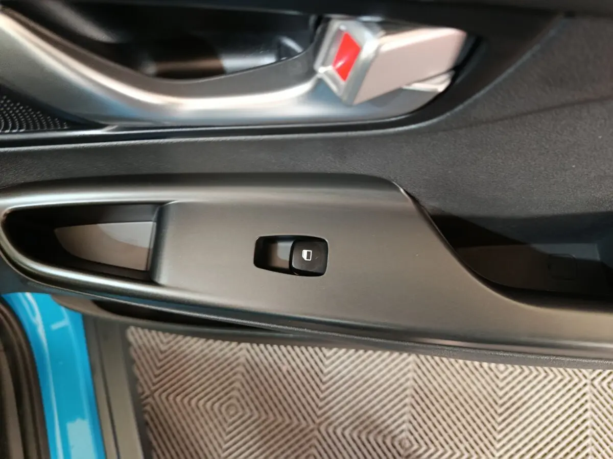 Gros plan sur le bouton de commande de la vitre électrique côté conducteur du Hyundai Kona bleu, avec poignée de porte noire.
