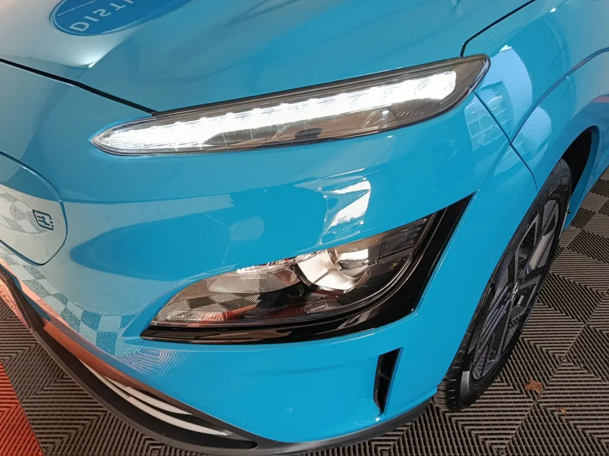 Gros plan sur l'avant droit bleu électrique du Hyundai Kona BEV 64kWh, mettant en valeur les phares LED et la roue.