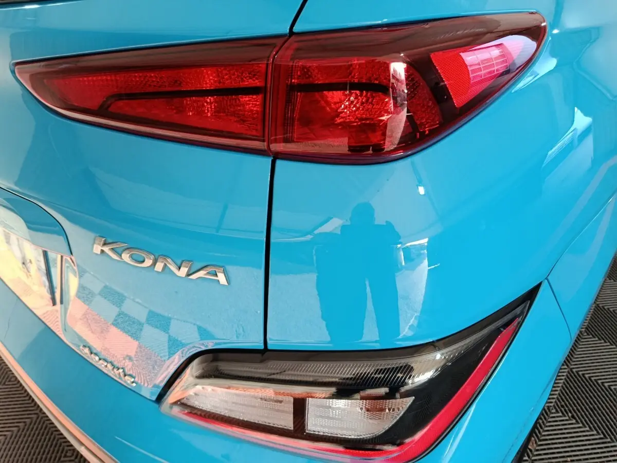 Gros plan sur le feu arrière droit et le logo KONA d’une Hyundai Kona électrique bleue, vue arrière côté droit.