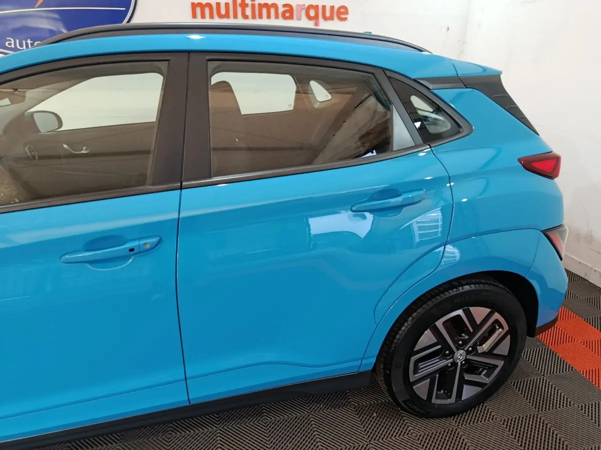 Vue latérale côté droit du Hyundai Kona électrique bleu, mettant en valeur les portes arrière et la roue arrière.