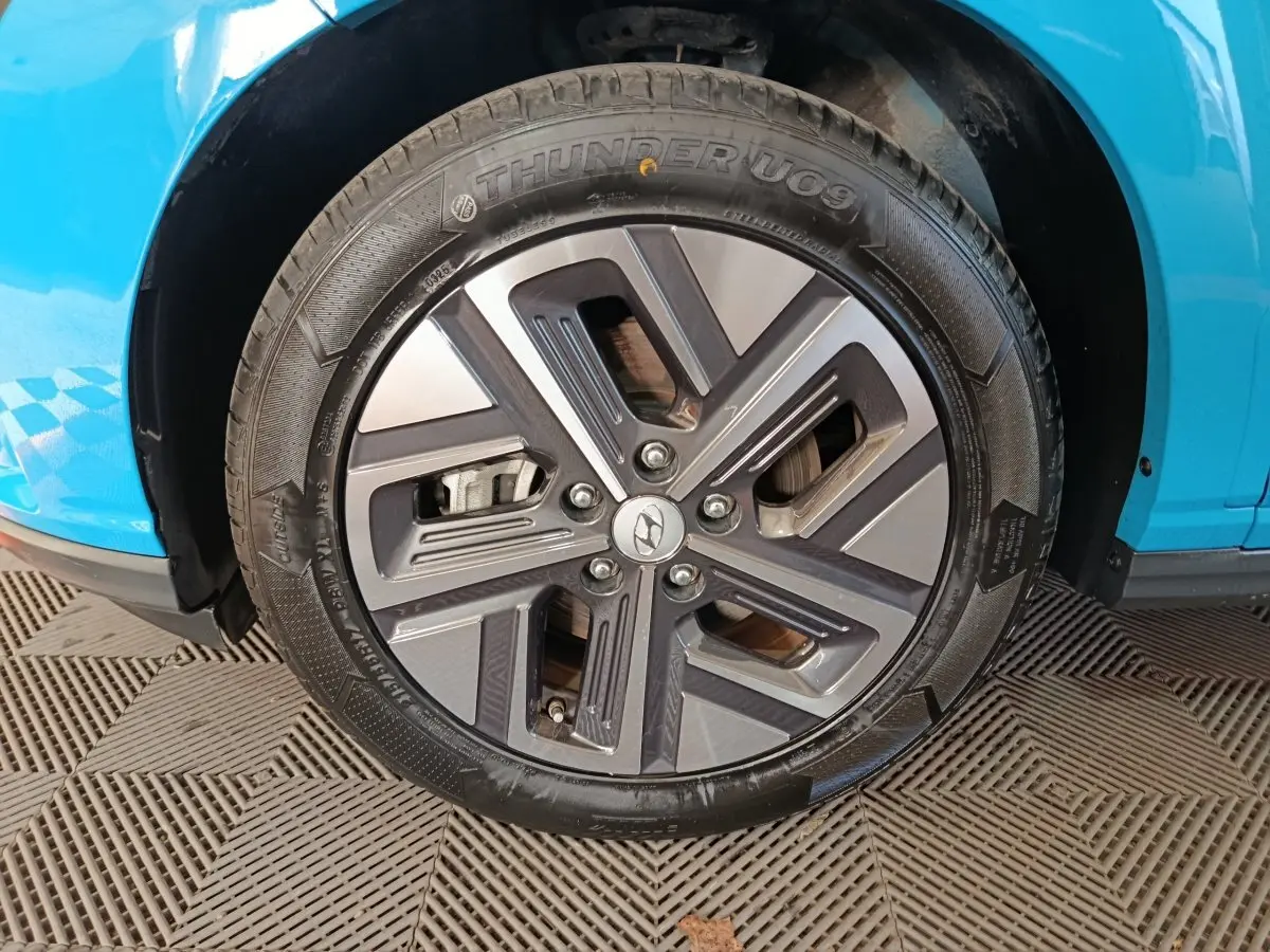 Gros plan sur la roue avant droite du Hyundai Kona électrique bleu 2022 avec jante alliage au design moderne.