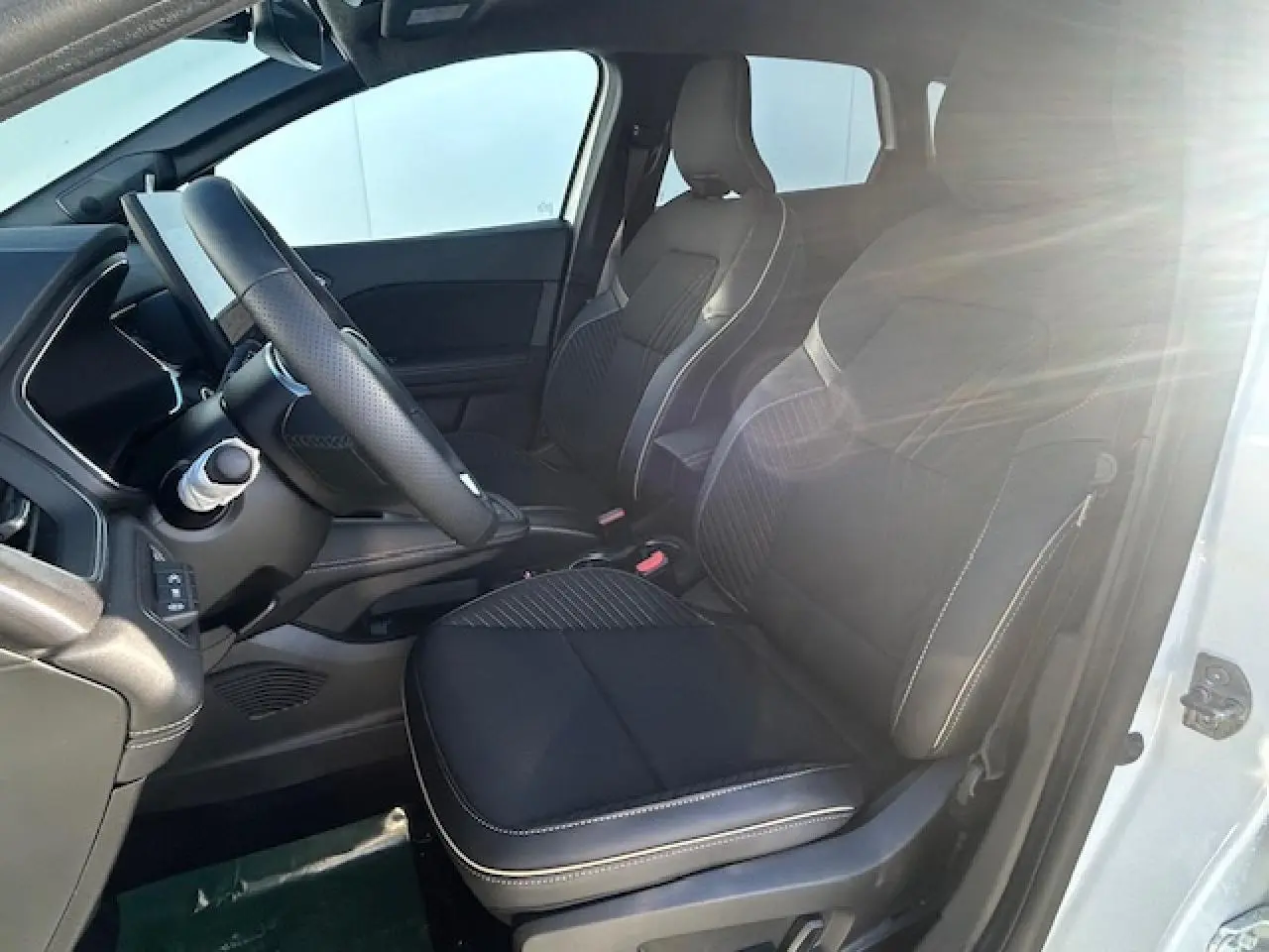 Vue intérieure côté conducteur d'une Renault SYMBIOZ blanc nacré, sièges noirs avec surpiqûres blanches et volant textile.