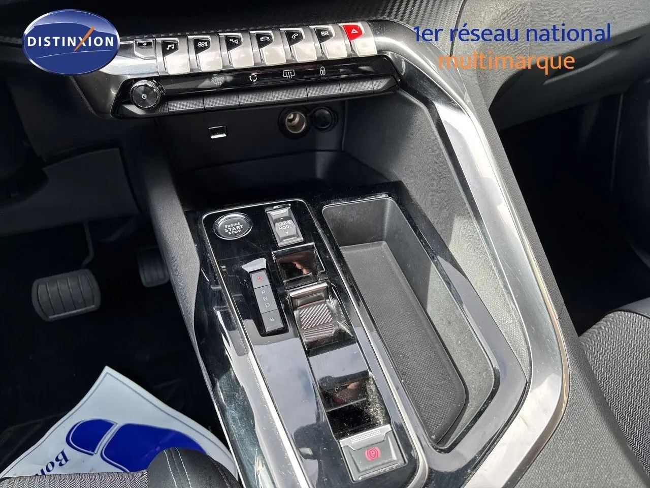 Vue rapprochée de la console centrale noire brillante du Peugeot 3008 Hybrid 2024 avec commandes et rangement.