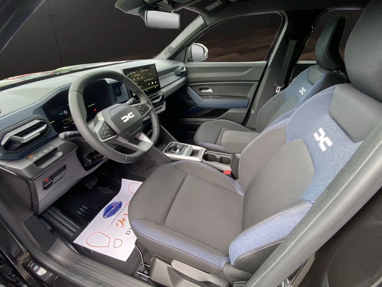 Intérieur avant droit du Dacia Duster hybride 2025, sièges tissu noir et bleu avec logo distinctif sur appuie-tête.
