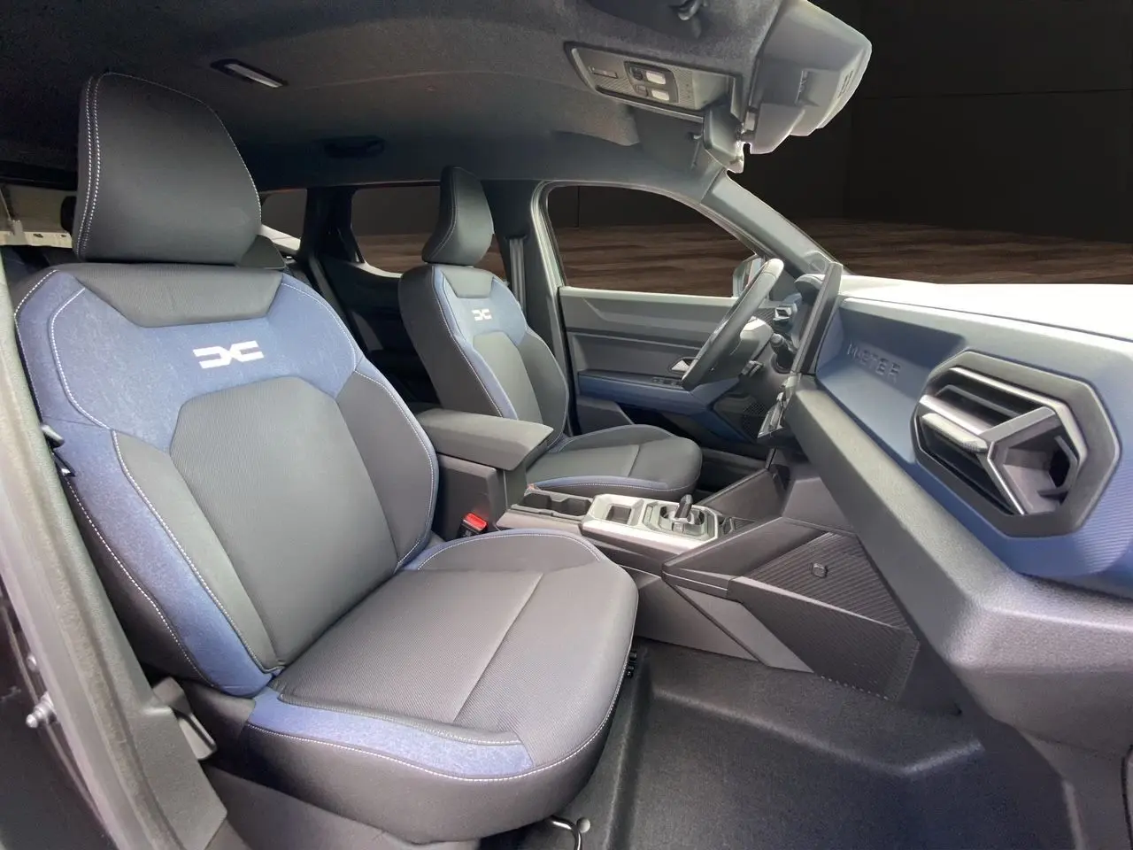 Vue intérieure côté conducteur du Dacia Duster hybride 2025, sièges tissu noir et bleu avec logo DC brodé.
