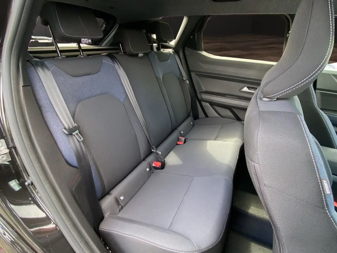 Vue intérieure côté droit des sièges arrière en tissu noir et bleu du Dacia Duster hybride 2025 avec portes ouvertes.