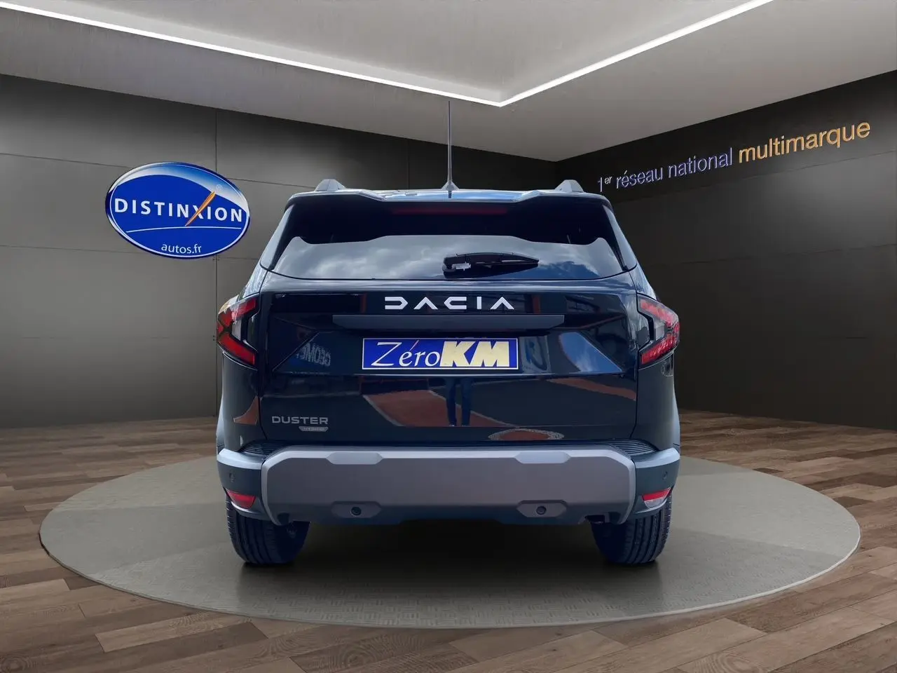 Vue arrière d'un Dacia Duster noir 2025 avec logo et plaque Zéro KM dans un showroom sombre.