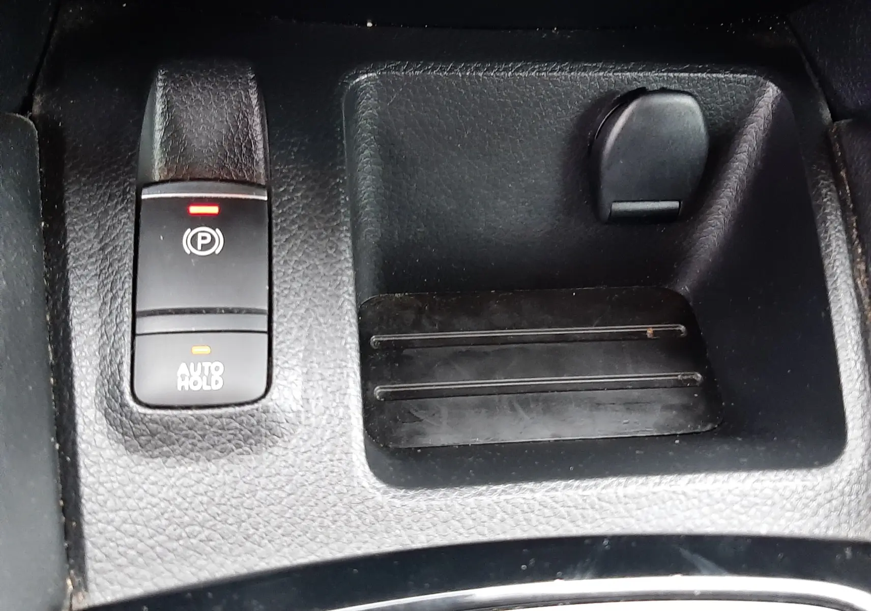 Gros plan sur la console centrale noire du Nissan Qashqai 2020, montrant le frein à main électrique et un espace de rangement.