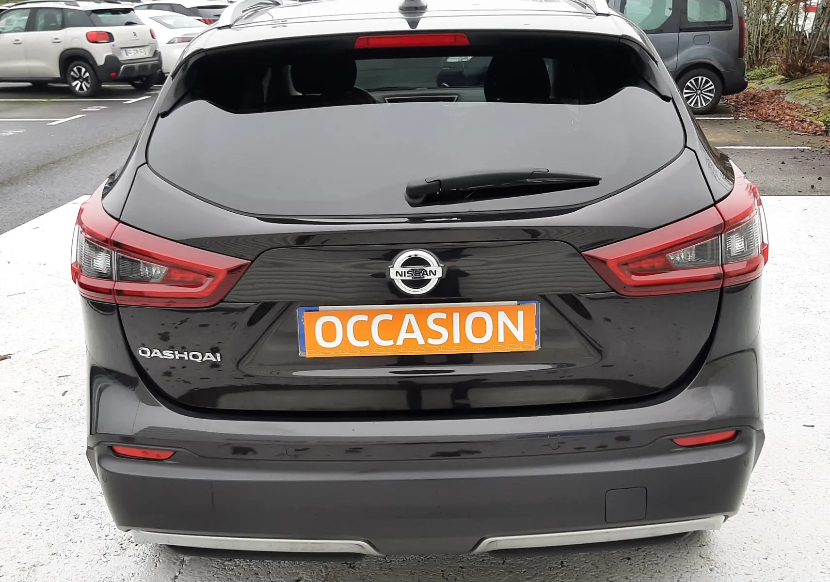 Vue arrière d'un Nissan Qashqai noir 2020 avec feux LED et plaque orange "OCCASION" sur un parking.