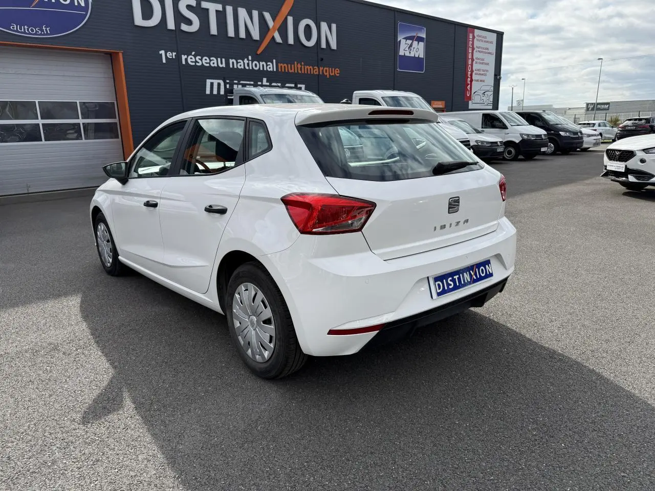 Vue 3/4 arrière droite d'une SEAT Ibiza blanche Candy 2019 avec jantes enjoliveurs et feux arrière distinctifs.