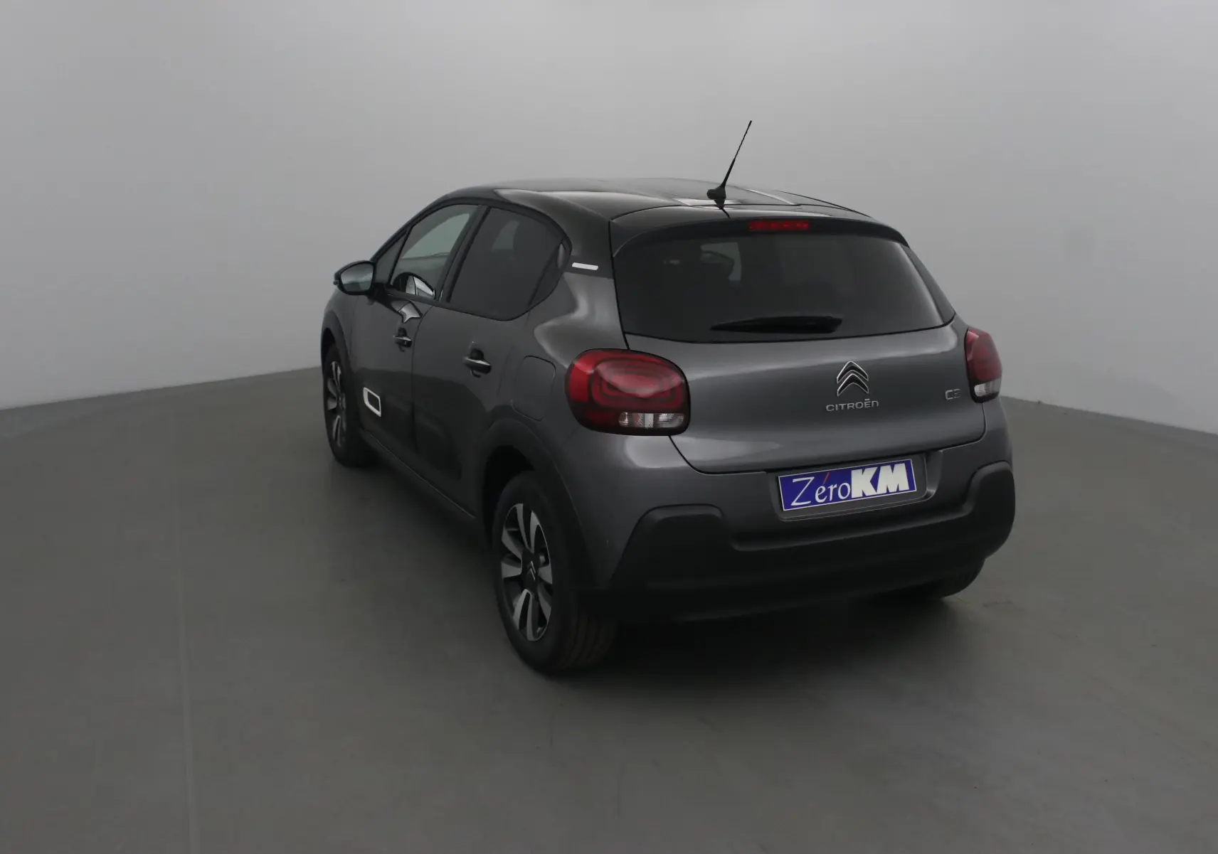 Vue 3/4 arrière gauche d'une Citroën C3 2022 gris platinium avec toit noir et feux arrière arrondis.