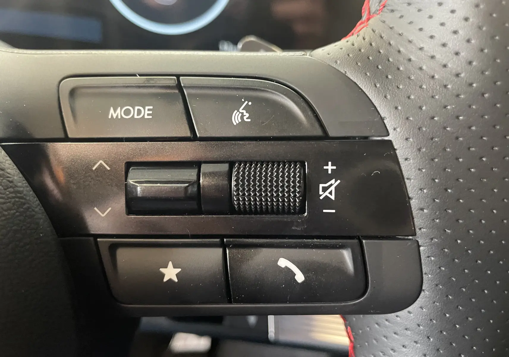Gros plan sur les commandes noires du volant perforé avec surpiqûres rouges du Hyundai Tucson 2025 hybride.