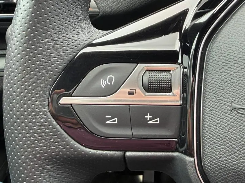 Gros plan sur les commandes de volume et de reconnaissance vocale à gauche du volant perforé du Peugeot 3008 Gris Platinium 2024.