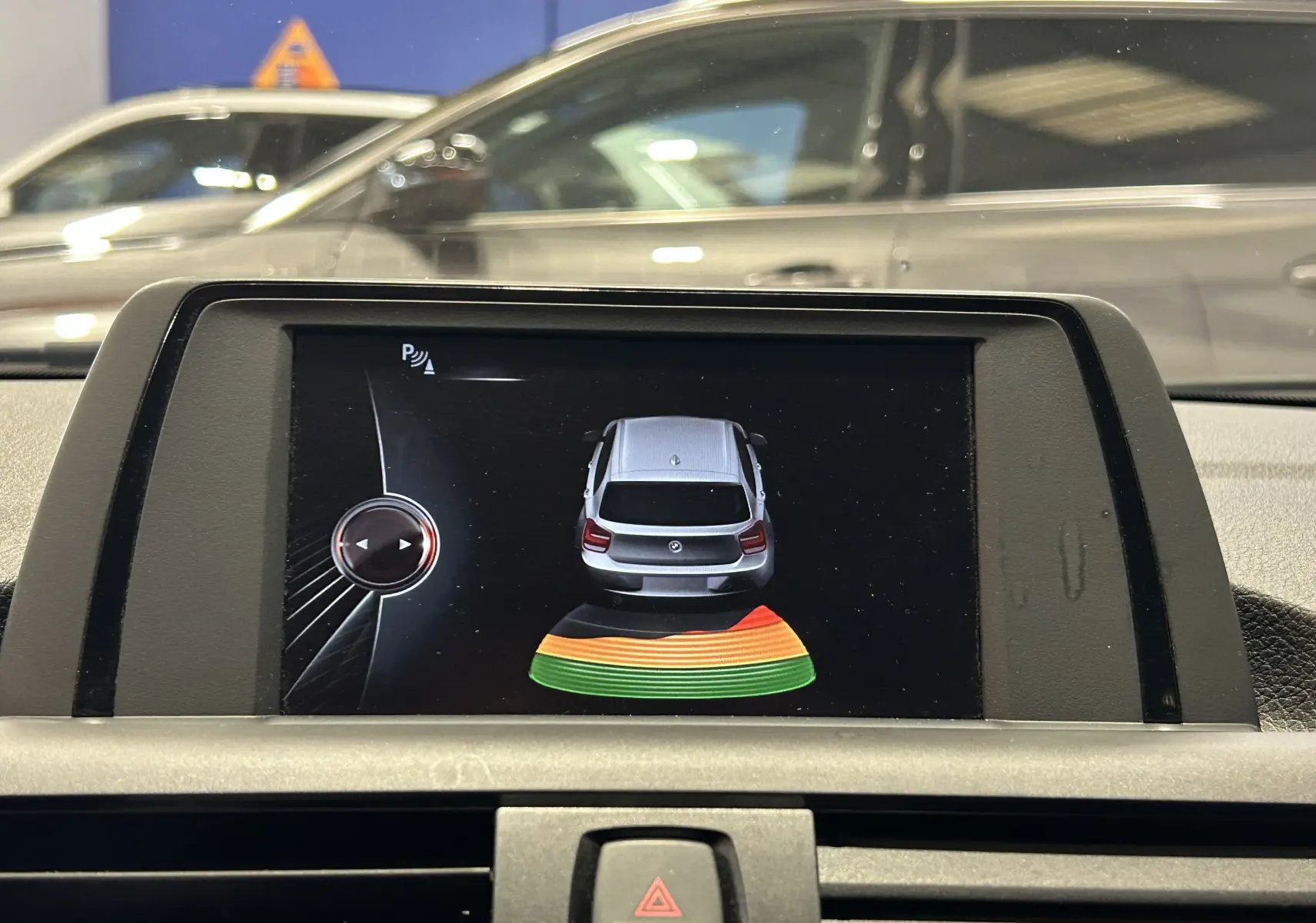Écran de la BMW Série 1 16d gris montrant l'alerte radar de recul avec visualisation arrière colorée.