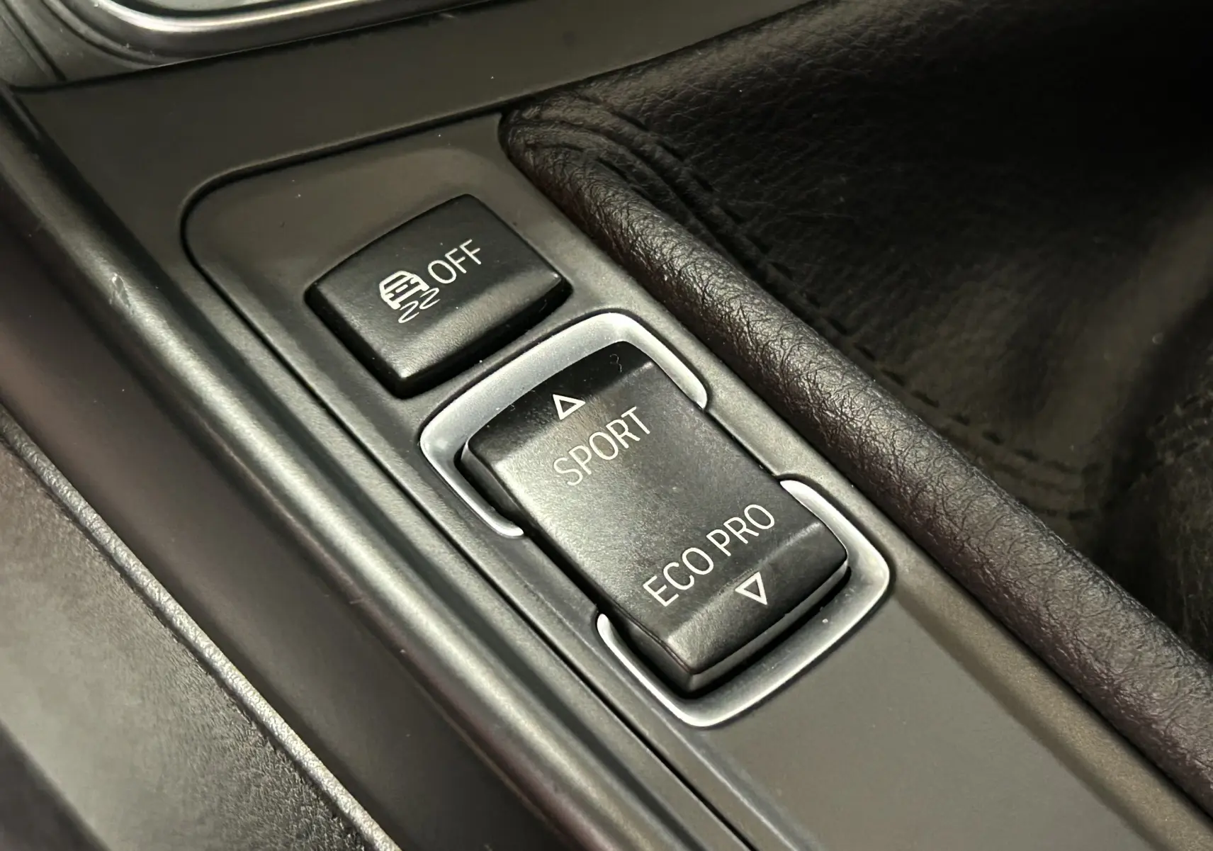 Gros plan sur les boutons de mode de conduite Sport et Eco Pro dans la console centrale d'une BMW Série 1 gris diesel.