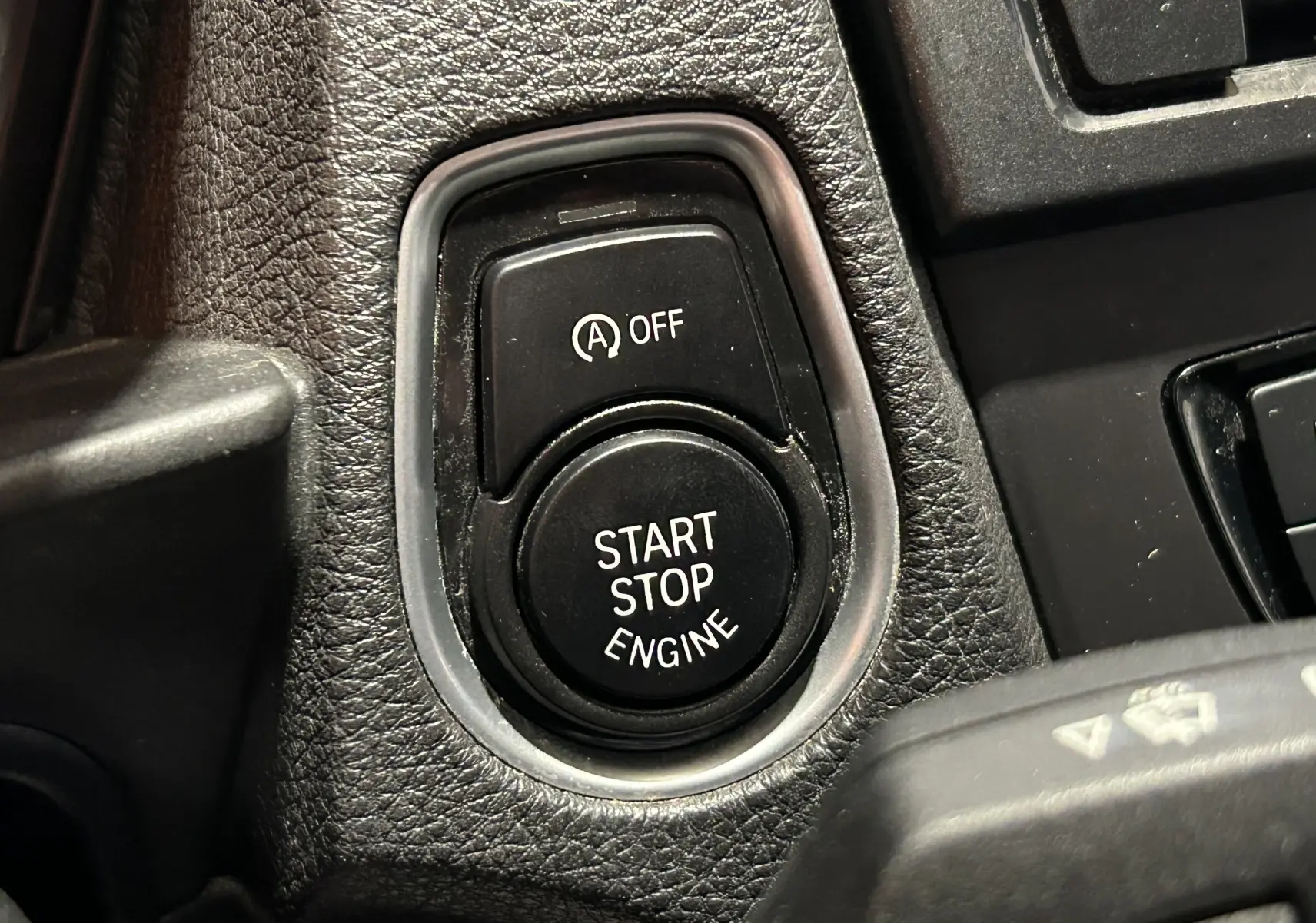 Gros plan sur le bouton Start Stop Engine et la commande d'arrêt automatique sur le tableau de bord noir d'une BMW Série 1 gris diesel.