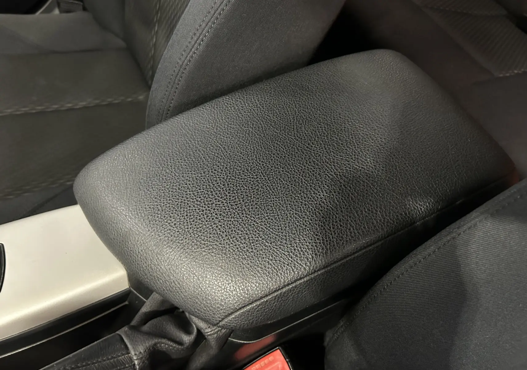 Gros plan sur l'accoudoir central en cuir noir et siège tissu côté conducteur d'une BMW Série 1 gris diesel 2014.