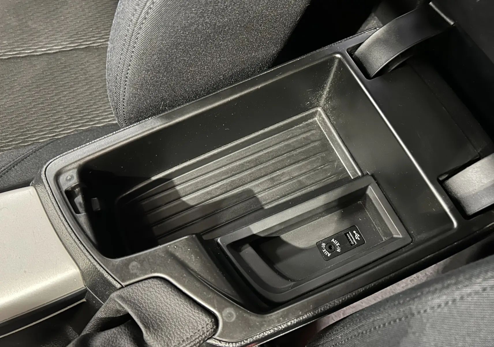 Gros plan sur la console centrale noire de la BMW Série 1 gris, montrant les ports USB et AUX entre les sièges avant.