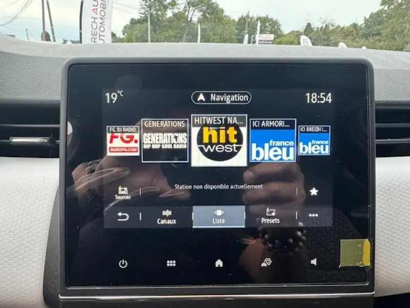 Écran tactile central affichant les stations radio dans l'habitacle d'une Renault Clio blanc glacier, vue de face.