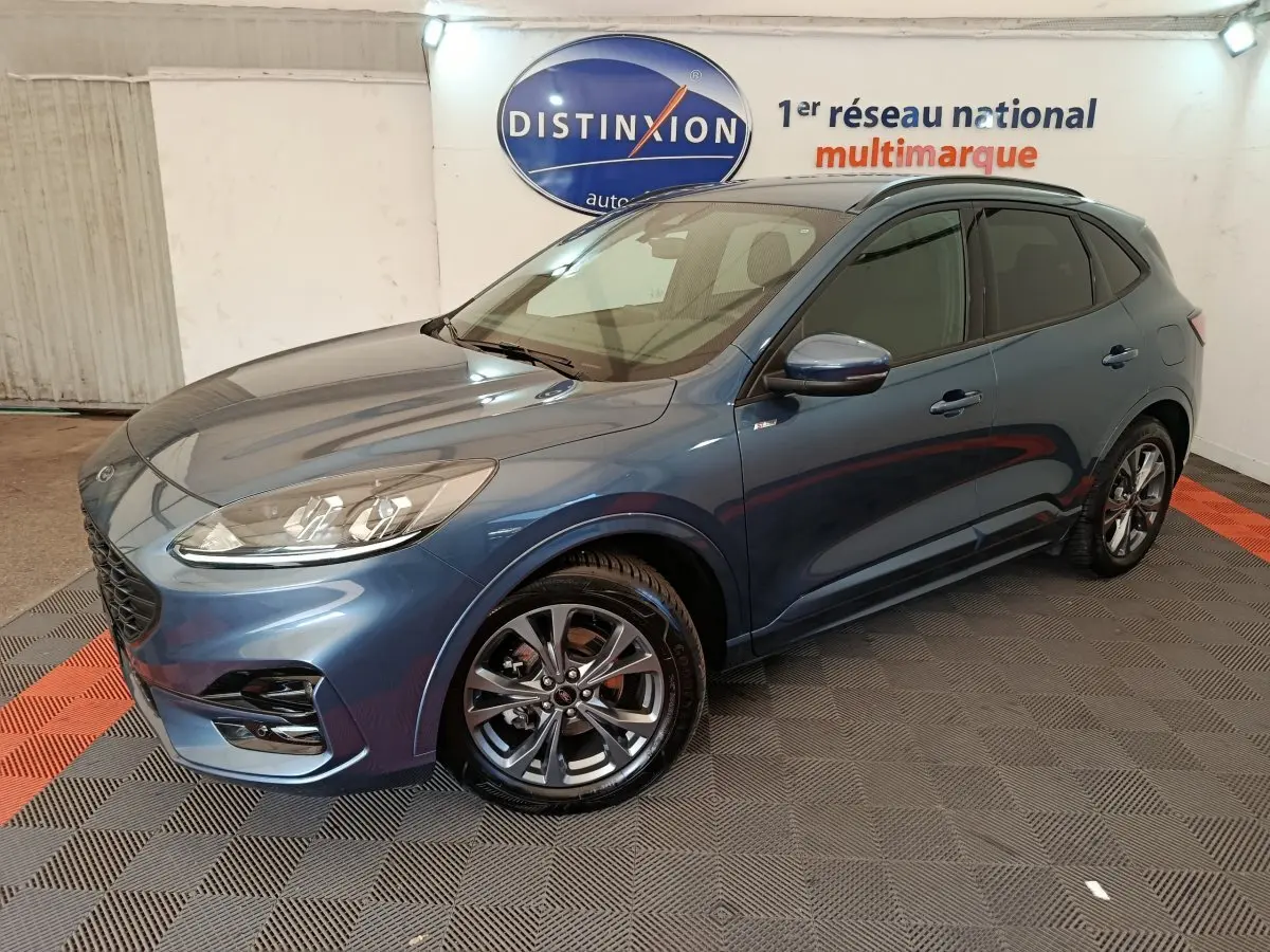 Ford Kuga 2024 bleu en vue 3/4 avant droit, avec jantes alliage et vitres teintées, dans un showroom intérieur.