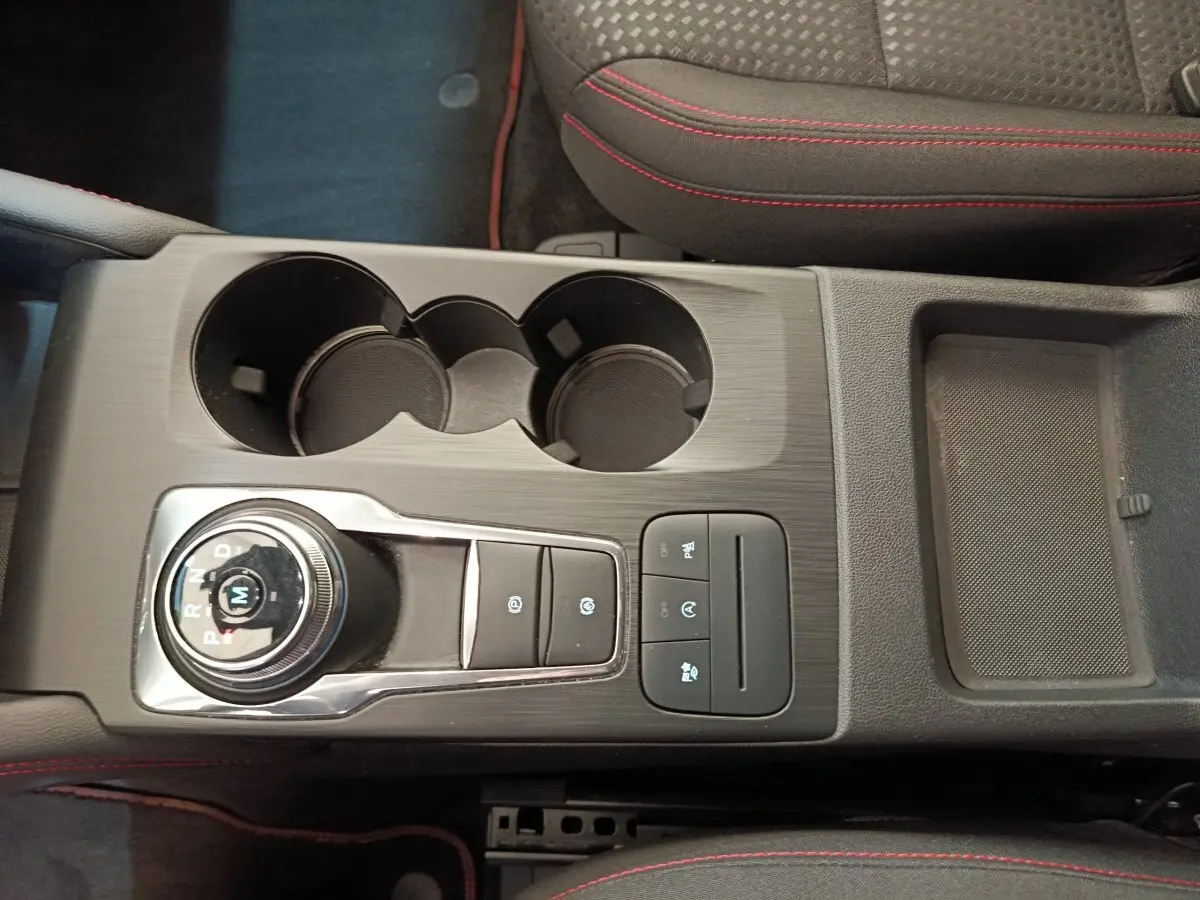 Vue plongeante sur la console centrale noire du Ford Kuga 2024 avec molette de boîte auto et surpiqûres rouges sur sièges.