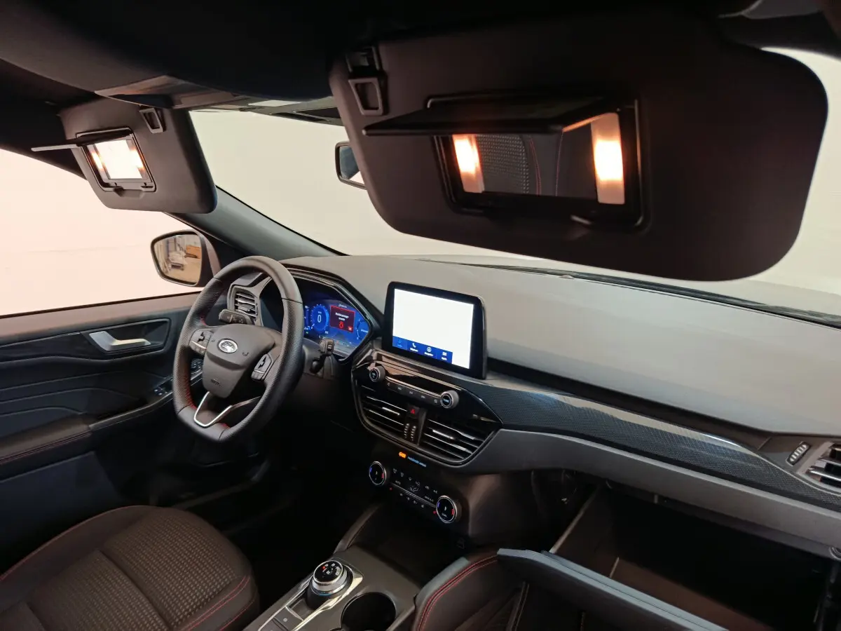 Vue intérieure côté conducteur du Ford Kuga 2024, tableau de bord noir avec écran tactile central et volant cuir multifonctions.