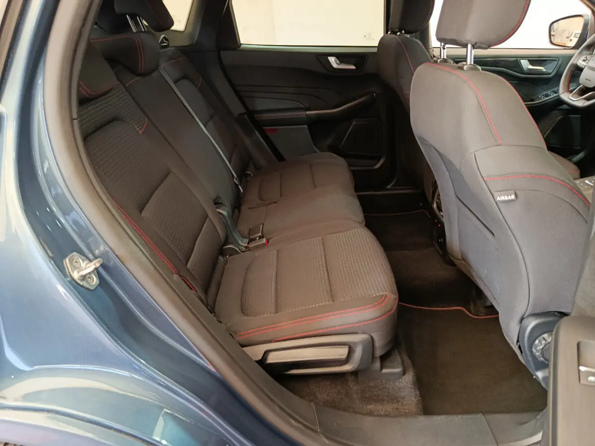 Vue intérieure côté gauche sur les sièges arrière noirs avec surpiqûres rouges du Ford Kuga bleu 2024 St Line.