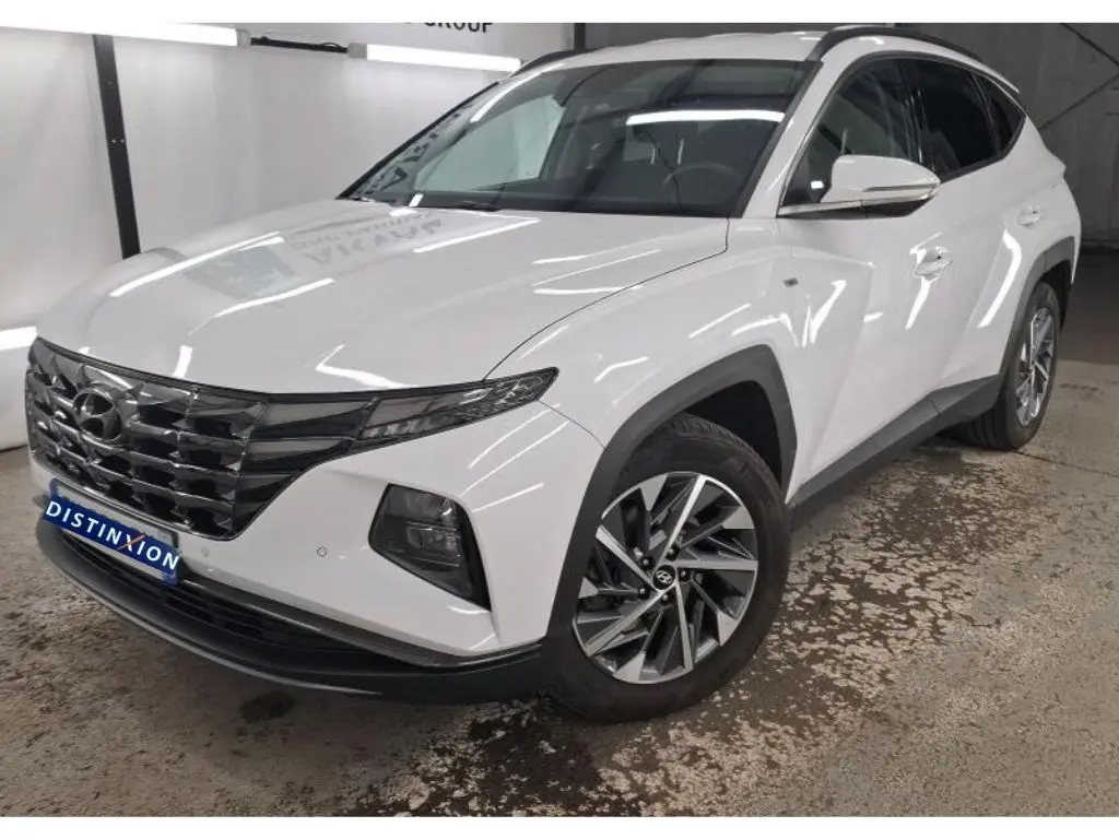 Hyundai Tucson blanc en 3/4 avant droit, avec jantes alliage et calandre chromée dans un showroom.