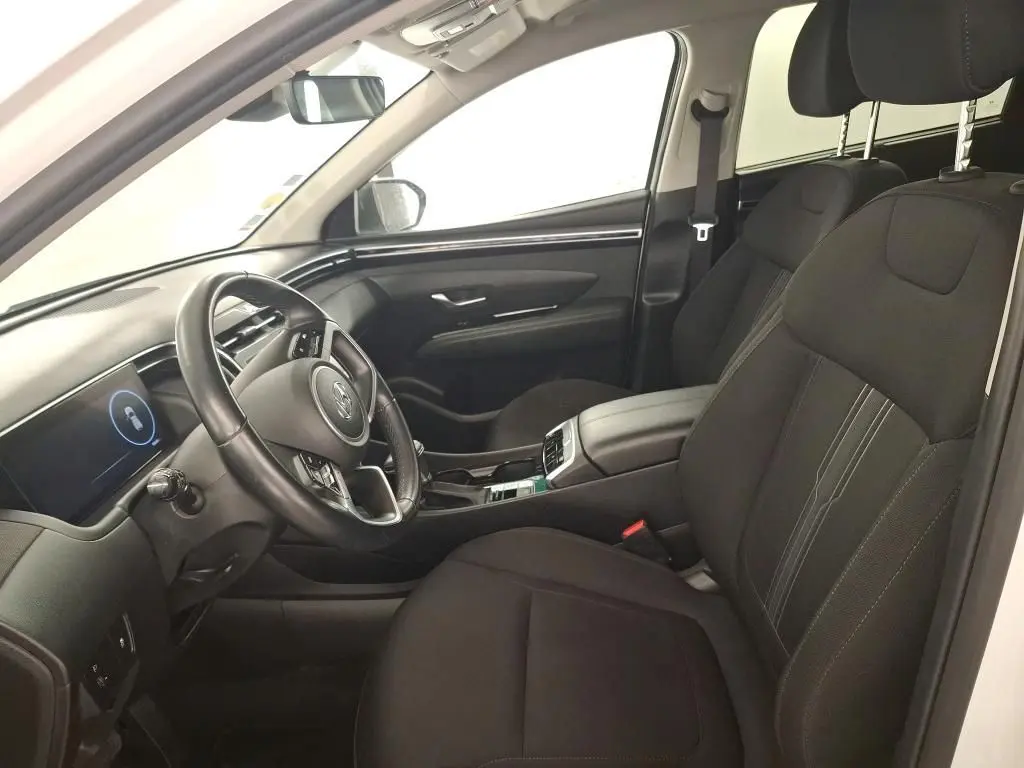 Vue 3/4 arrière droite d'un Hyundai Tucson blanc avec vitres teintées et jantes alliage, en intérieur showroom.