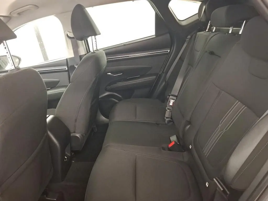 Vue intérieure côté conducteur du Hyundai Tucson blanc 2021, sièges noirs, volant multifonction et tableau de bord digital.