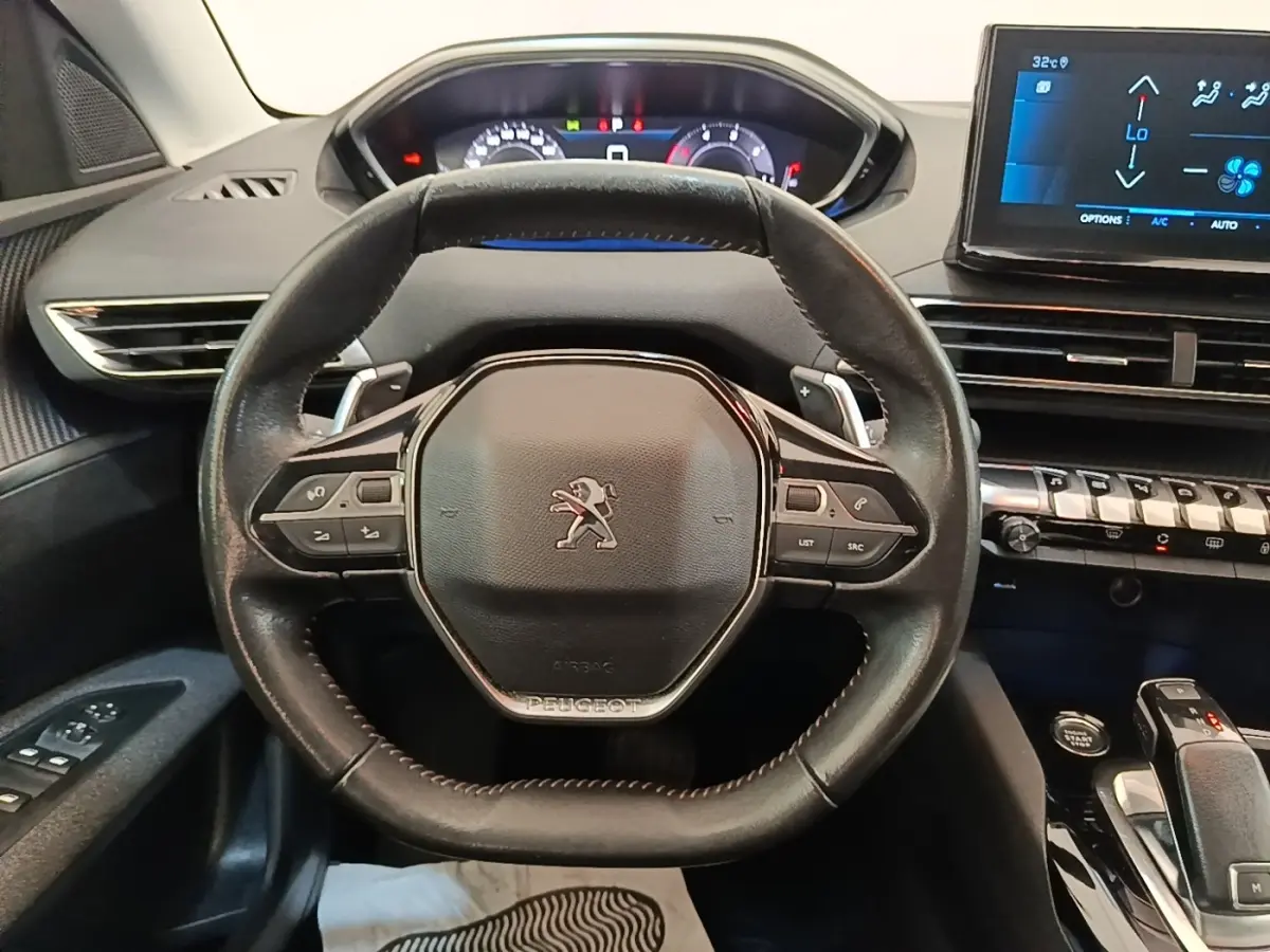Vue intérieure centrée sur le volant cuir multifonctions d'une Peugeot 3008 2022 avec tableau de bord digital et écran tactile.