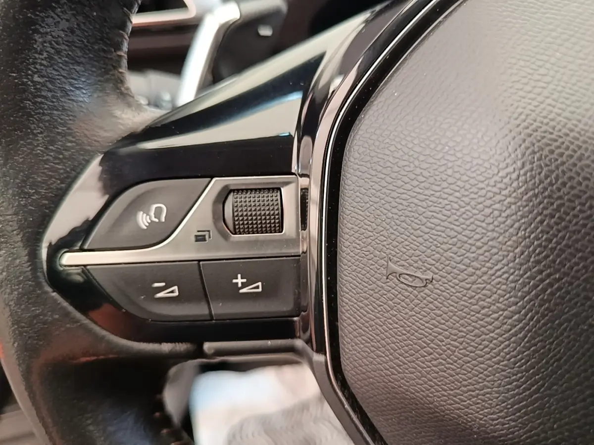Gros plan sur le volant cuir noir multifonctions du Peugeot 3008 2022, avec commandes vocales et réglages de volume.