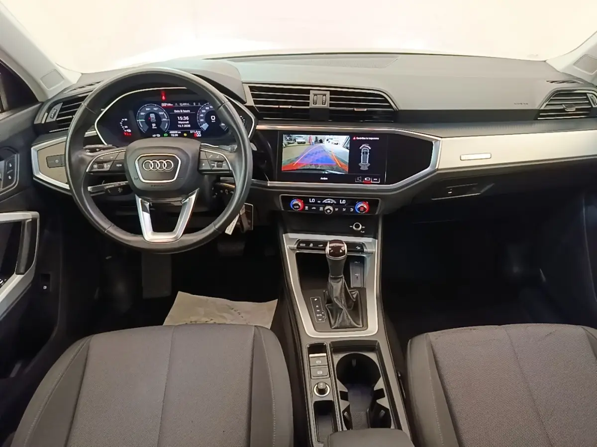 Vue intérieure avant de l'Audi Q3 45 TFSI e 2023, tableau de bord avec écran tactile et volant cuir multifonctions.