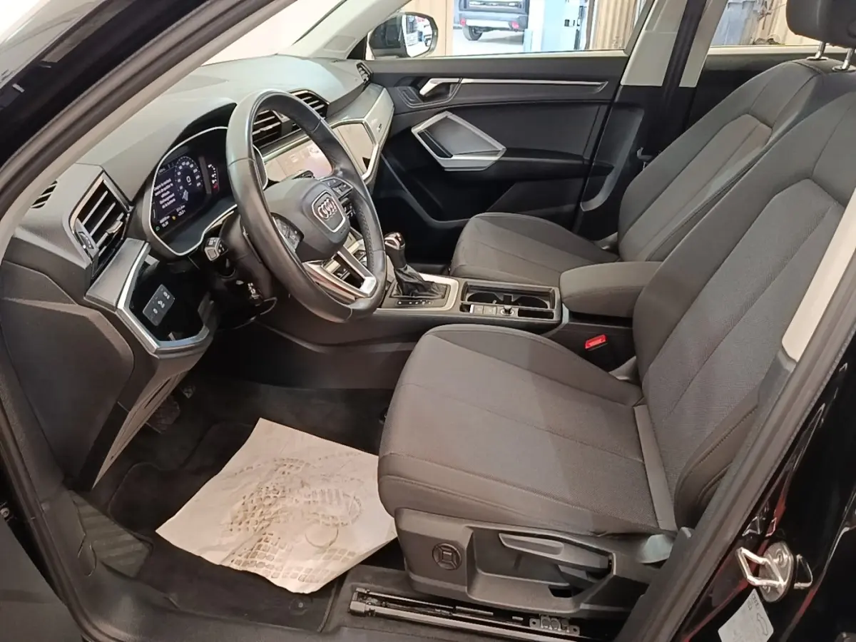 Intérieur avant droit de l'Audi Q3 45 TFSI e 2023 avec sièges gris, volant cuir multifonctions et tableau de bord digital.