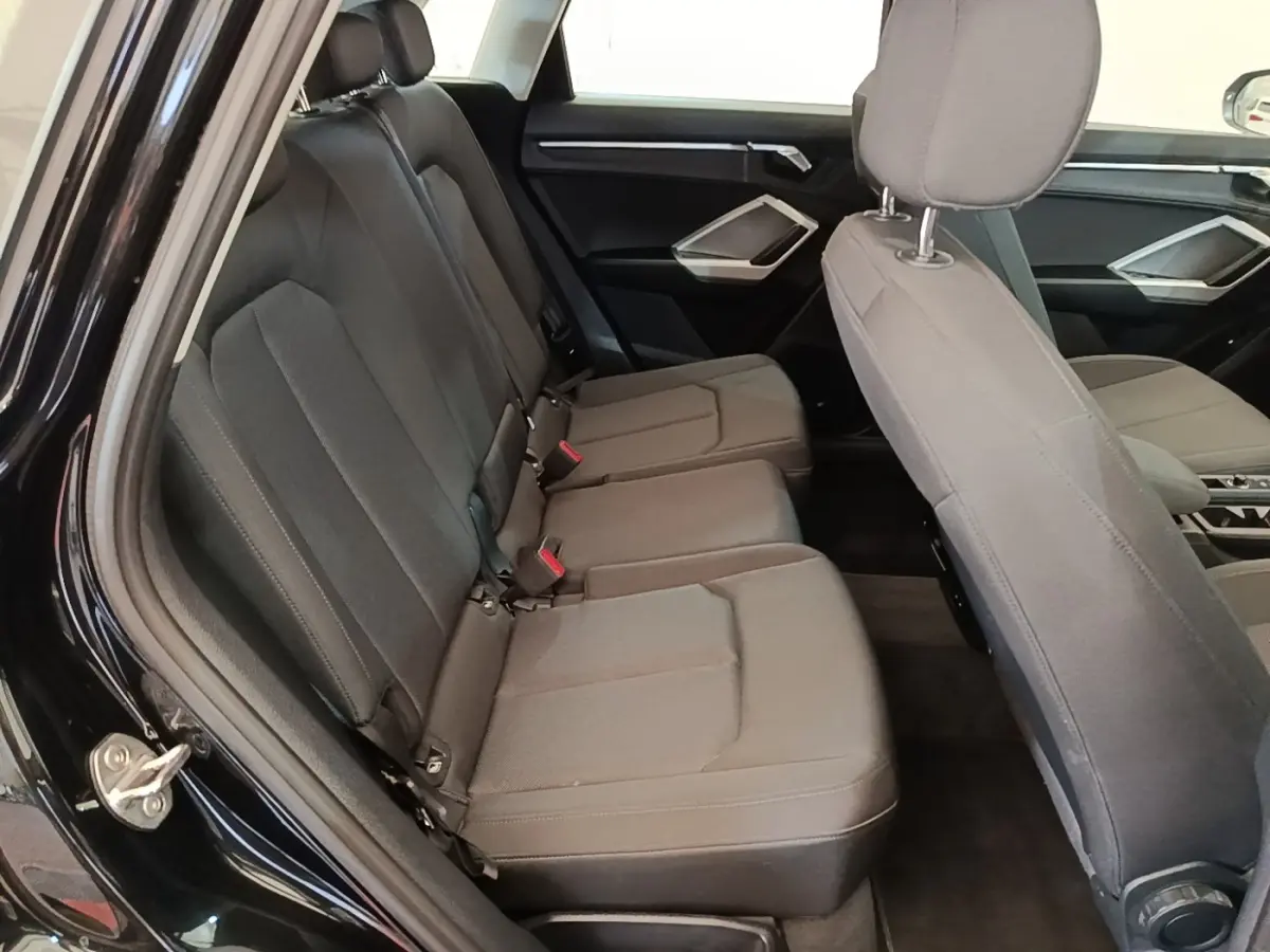 Vue intérieure côté gauche montrant la banquette arrière grise et les sièges avant du SUV Audi Q3 hybride 2023.