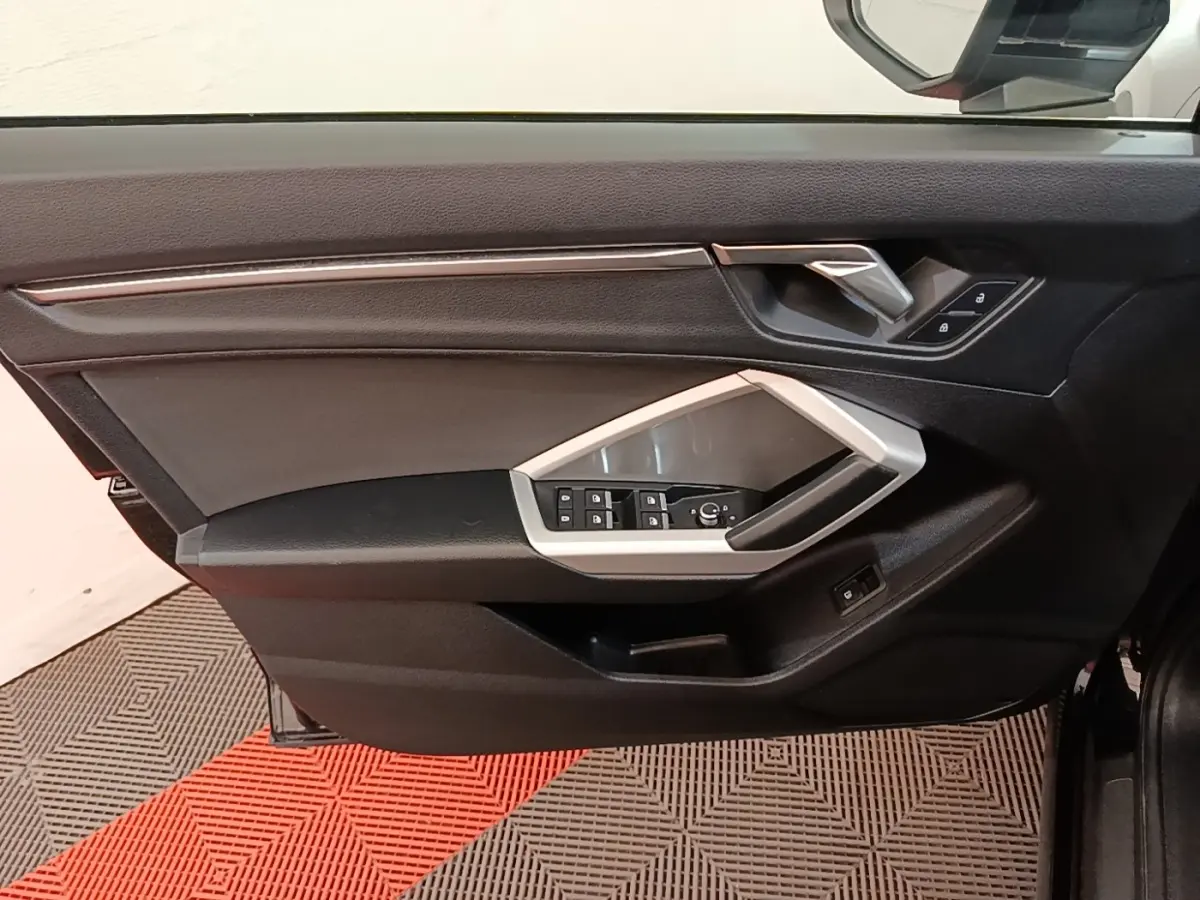 Vue intérieure côté gauche de la porte avant d'un Audi Q3 2023, avec commandes électriques et garniture noire.