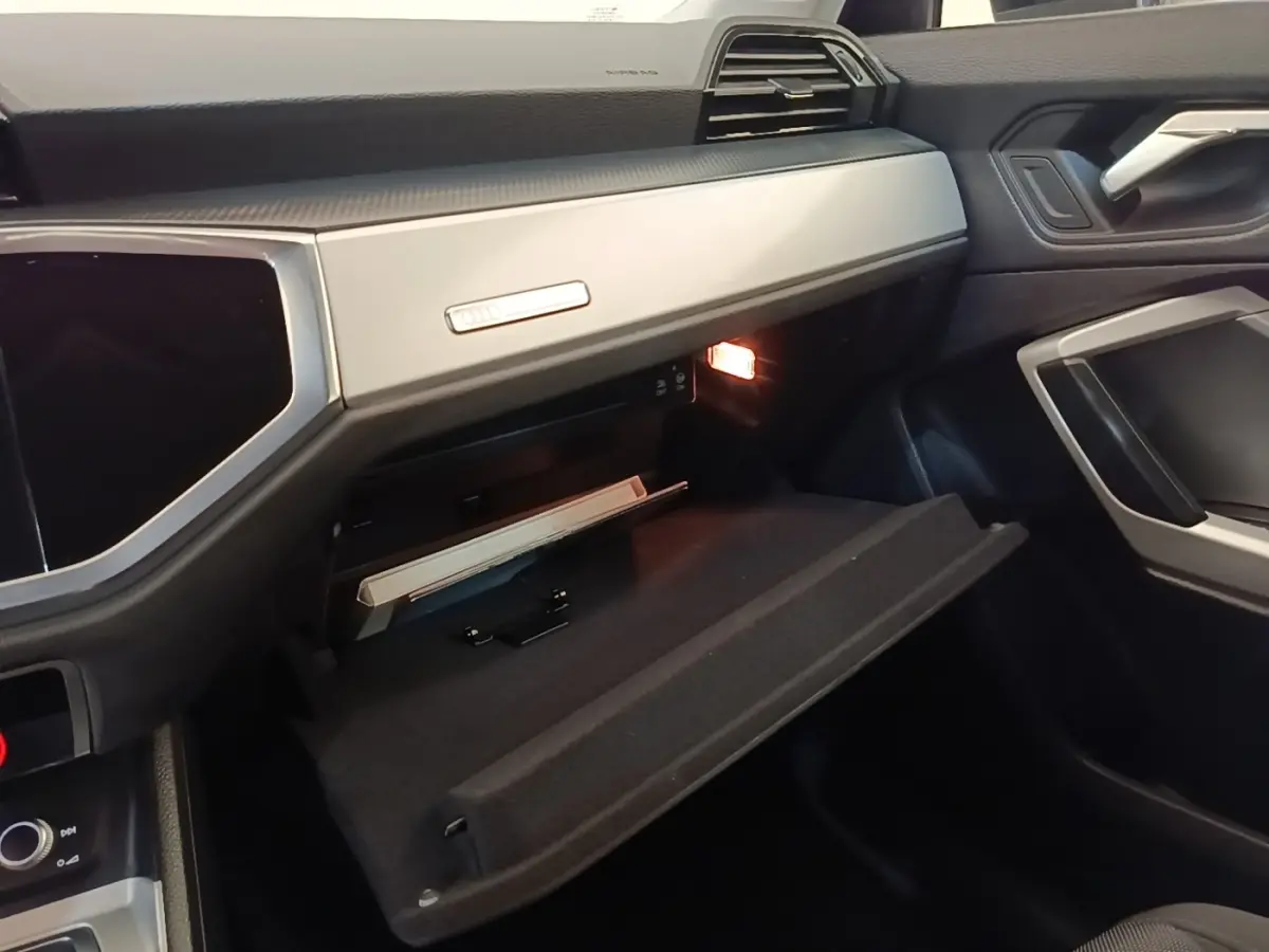 Intérieur Audi Q3 2023 vue côté passager, boîte à gants ouverte avec éclairage et tableau de bord gris clair.