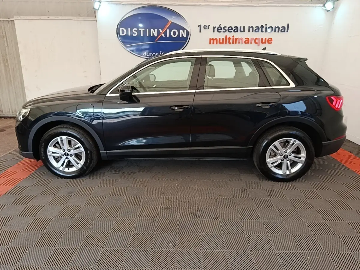 Vue de profil côté gauche d’un Audi Q3 hybride rechargeable 2023 noir avec jantes argentées en intérieur showroom.