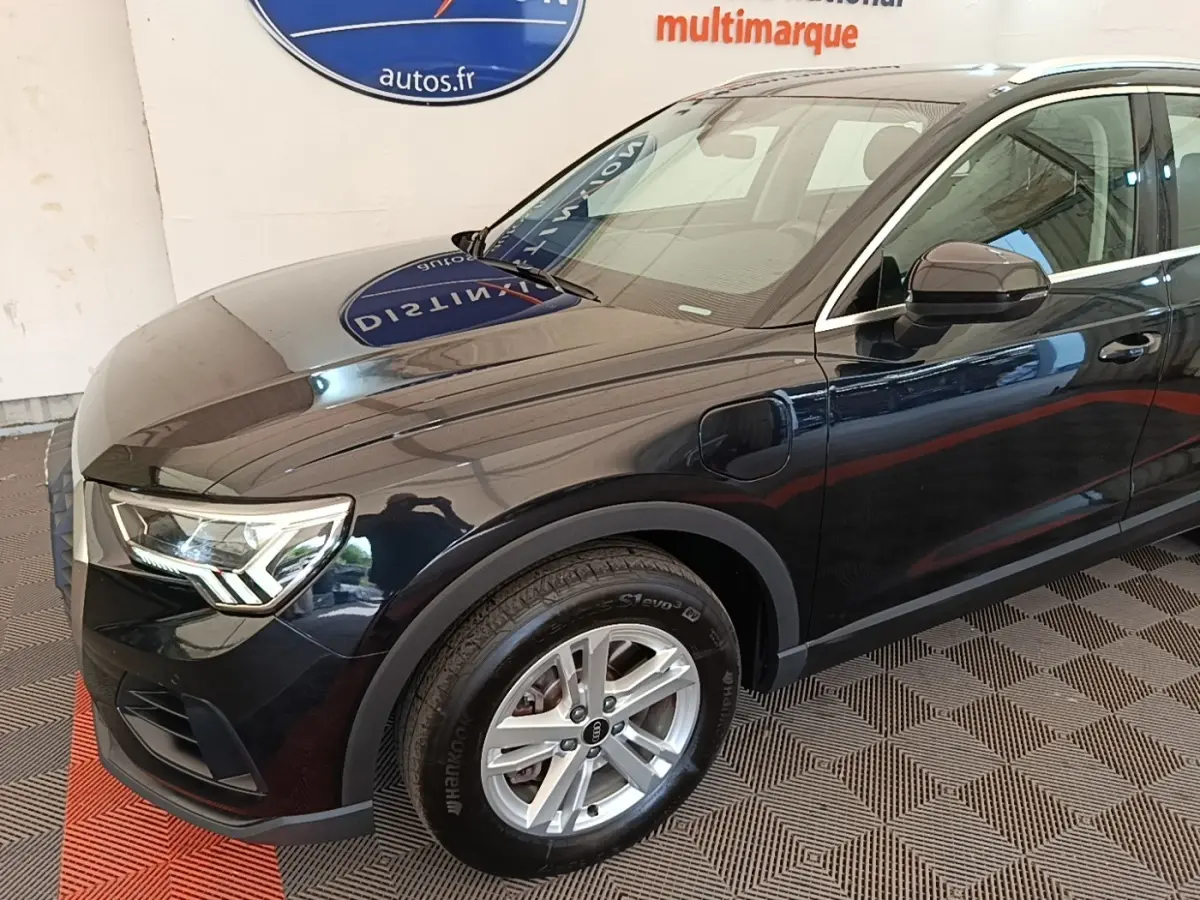 Vue 3/4 avant droit d’un Audi Q3 hybride rechargeable noir avec jantes alliage et prises de recharge visibles sur l’aile avant.