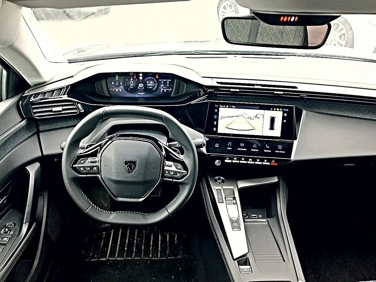 Vue intérieure frontale du tableau de bord et volant cuir noir de la Peugeot 408 Hybrid 145 allure 2024 avec écran tactile et caméra de recul affichée.