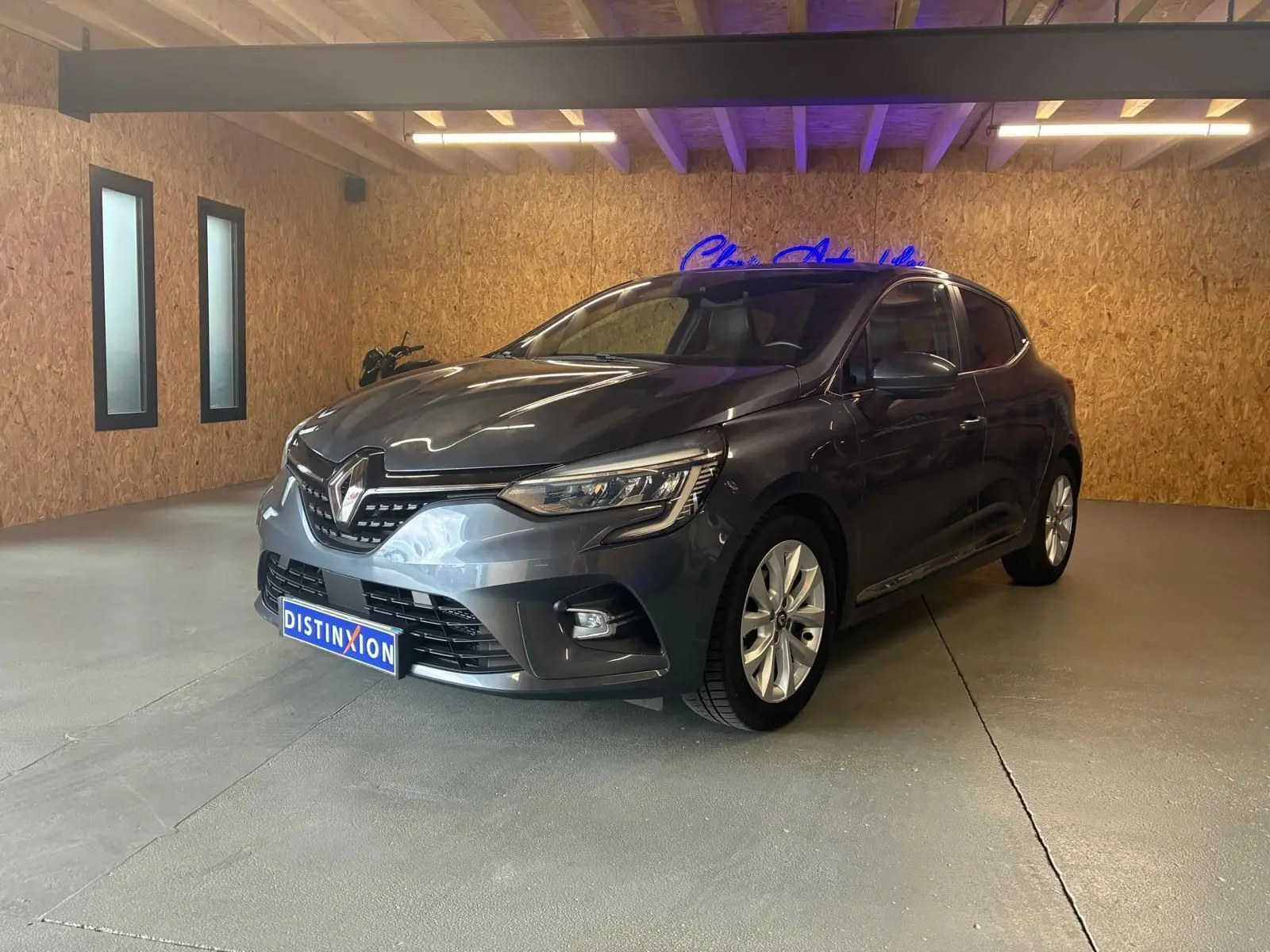 Renault Clio 1.0 TCE 100 Intens gris vue 3/4 avant droit en intérieur avec jantes alliage et phares LED.