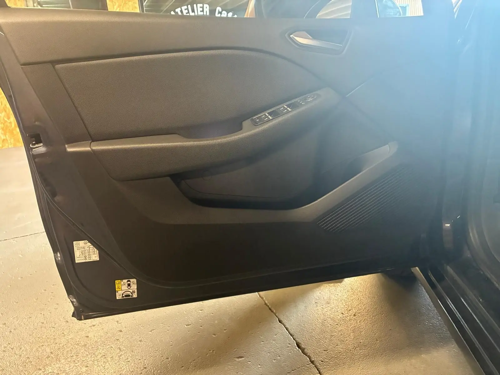 Porte avant gauche ouverte d'une Renault Clio gris 2020, montrant les commandes de vitre et le panneau intérieur noir.