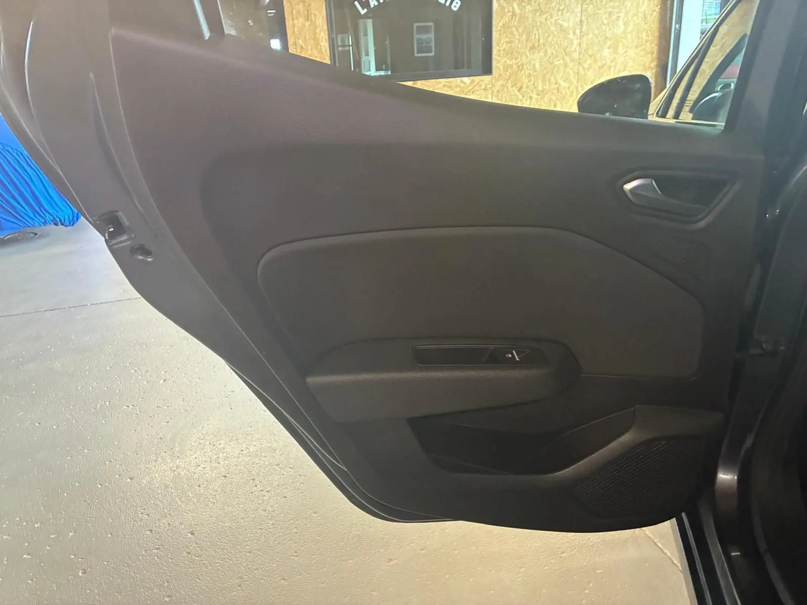 Gros plan sur la porte intérieure côté gauche d'une Renault Clio gris 2020, avec commande de vitre et tissu noir.