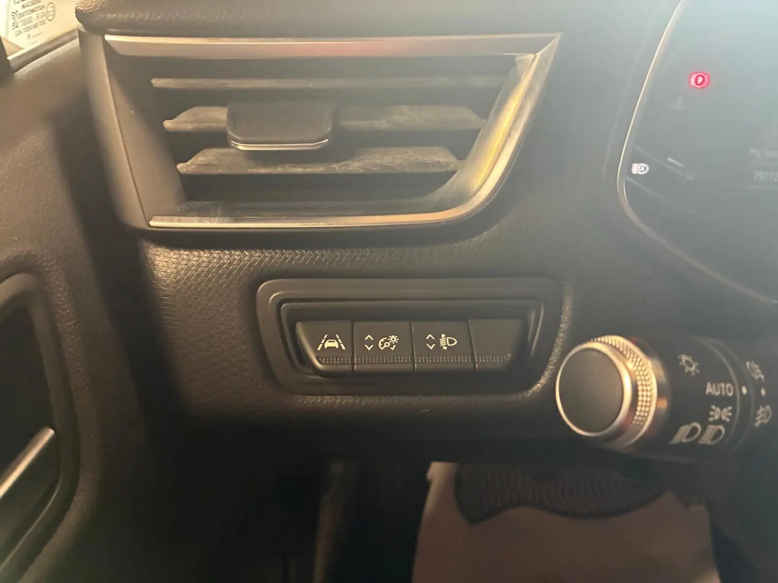 Gros plan sur les commandes d'assistance et de réglage des phares à gauche du volant dans l'habitacle gris-noir d'une Renault Clio 2020.