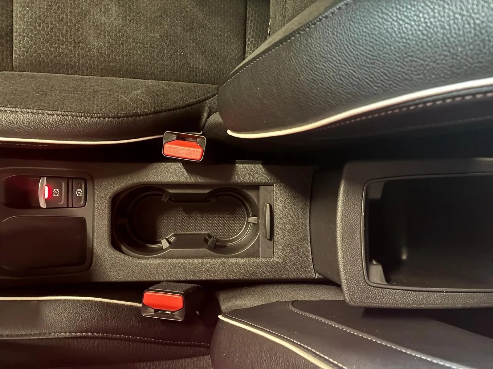 Vue rapprochée de la console centrale de la Renault Clio 2020 gris, avec porte-gobelets et ceintures rouges visibles.