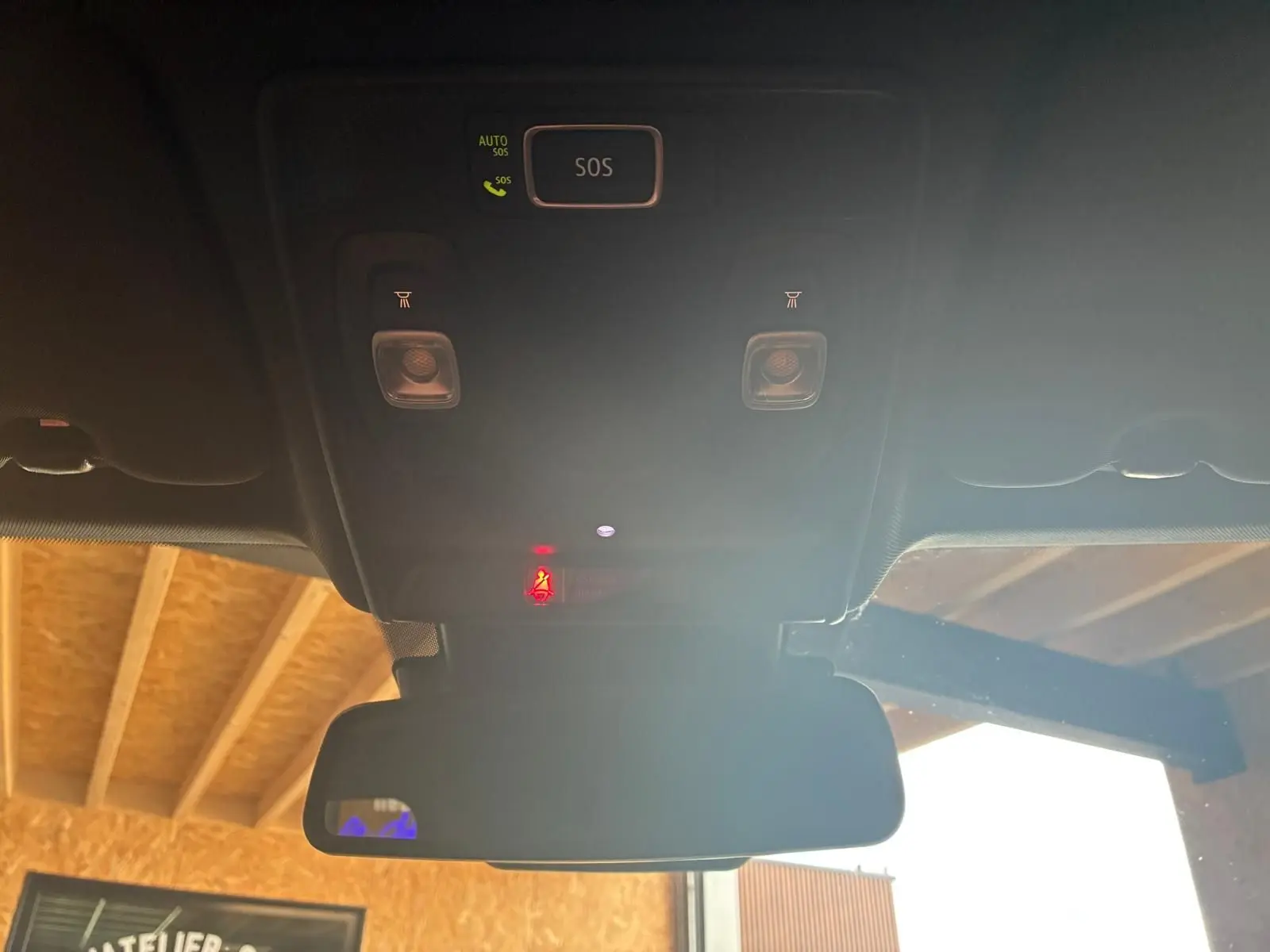 Vue intérieure du plafond avec boutons SOS et éclairages, rétroviseur et partie du toit en bois visible à l'extérieur.