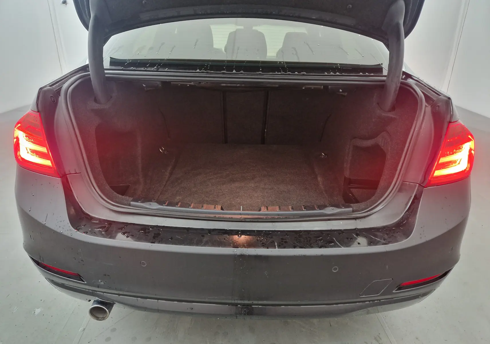 Vue arrière d'une BMW Série 3 316D noire de 2014 avec coffre ouvert et feux arrière allumés dans un garage.