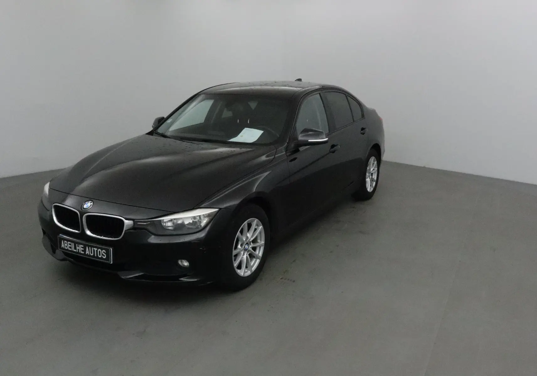 BMW Série 3 316D noire vue en 3/4 avant droit dans un studio, avec jantes alliage et calandre chromée.