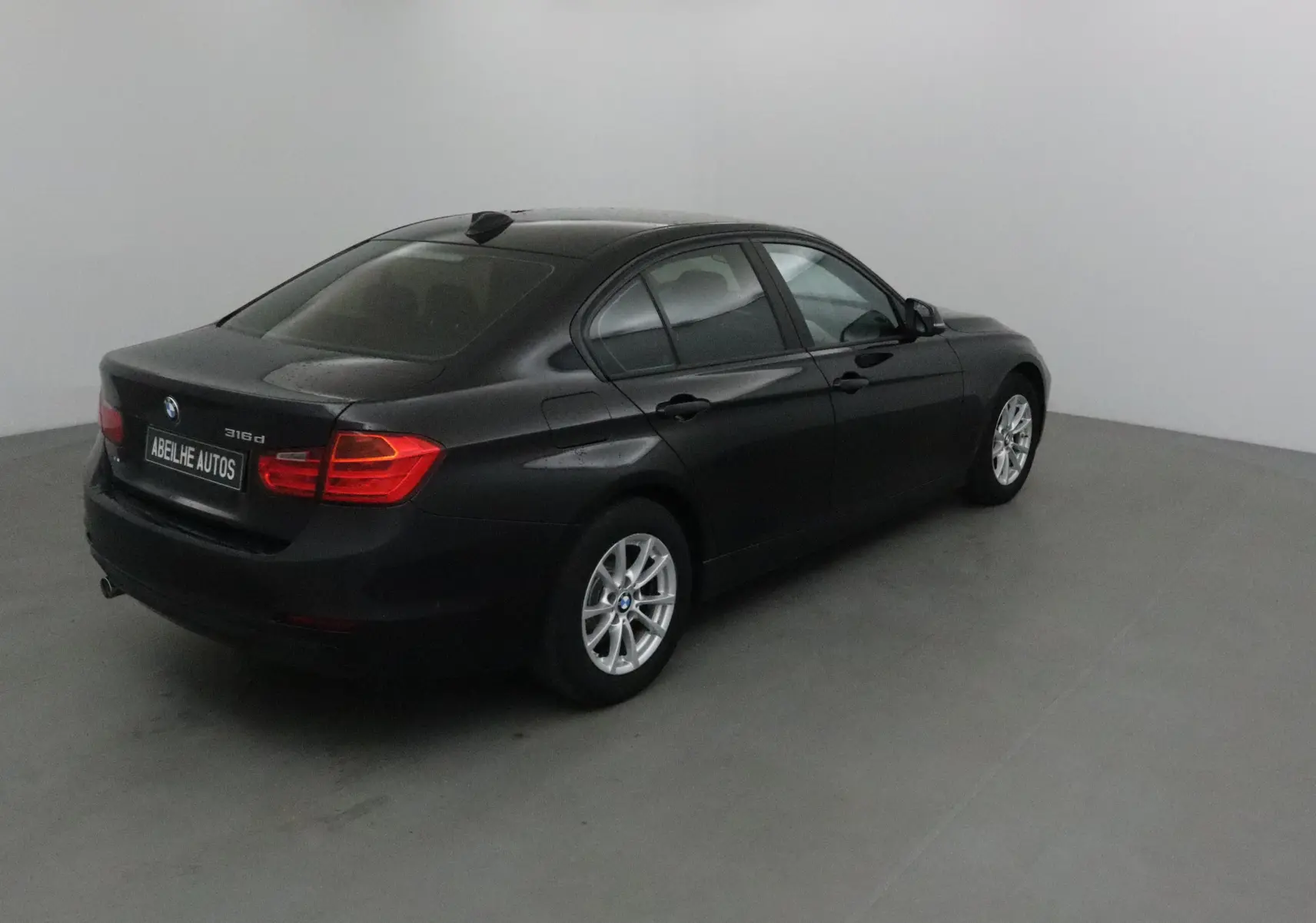 BMW Série 3 316d noire vue en 3/4 arrière droit, avec jantes alliage et feux arrière allumés.