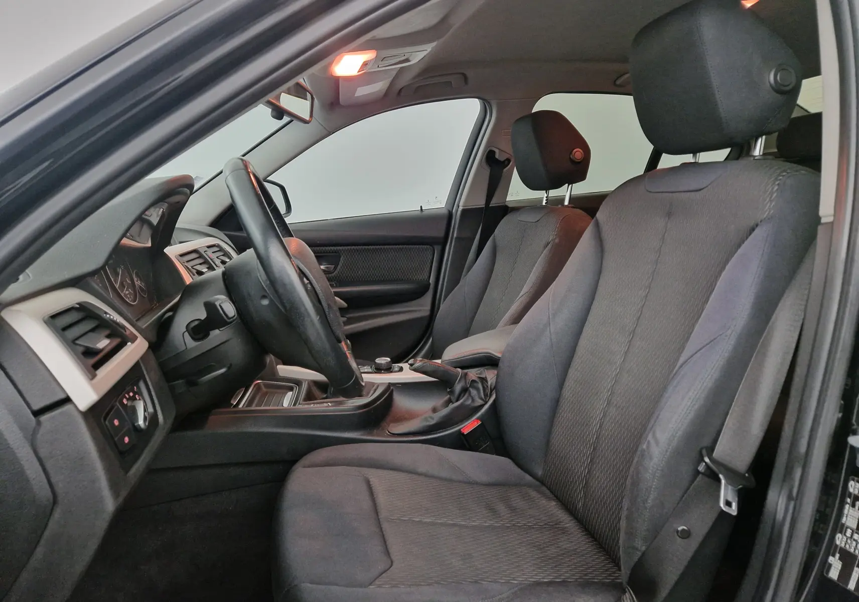 Vue intérieure côté conducteur de la BMW Série 3 316D noire, mettant en valeur les sièges tissu et la boîte manuelle.